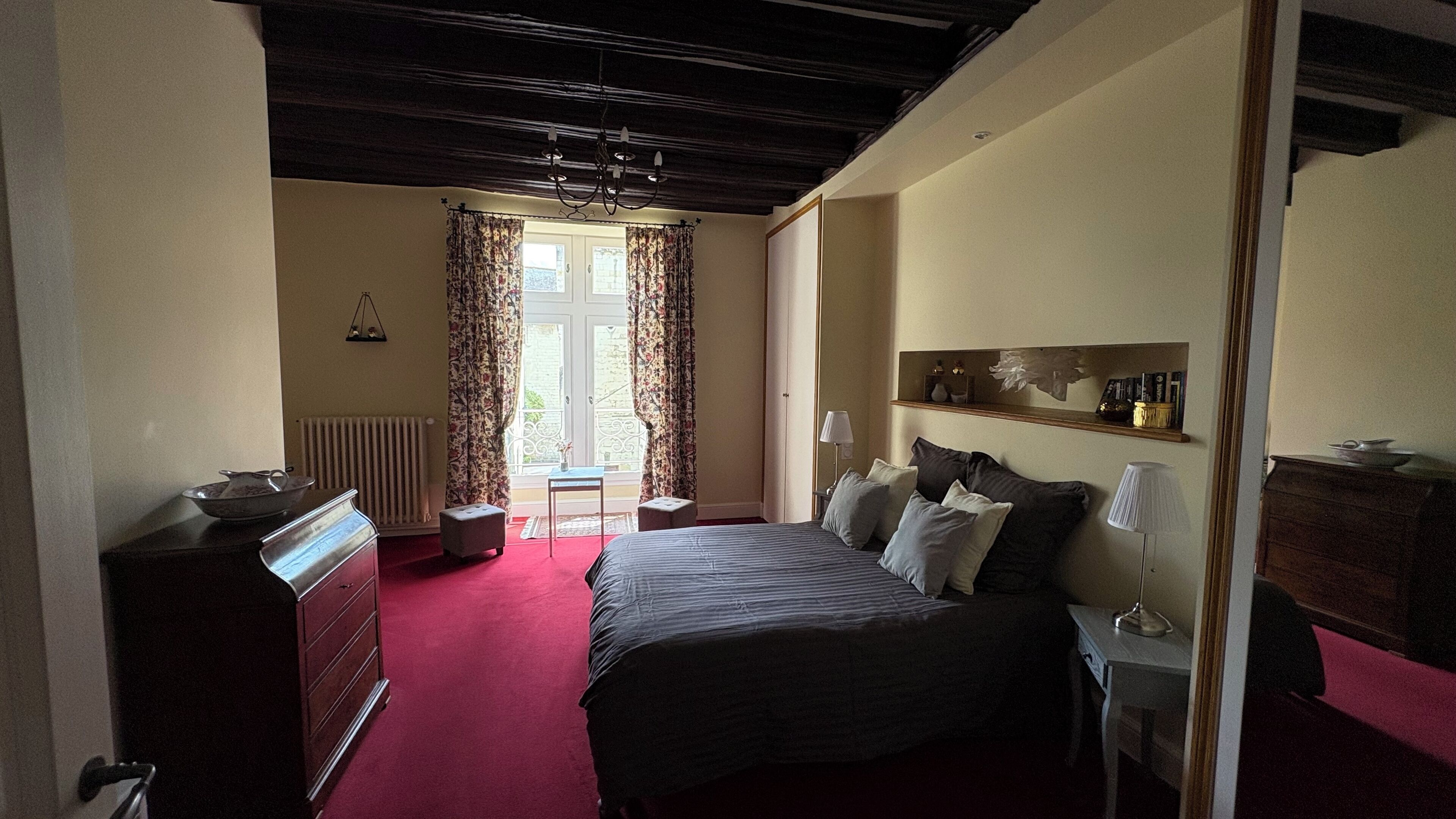 Een slaapkamer met een bed, dressoir, radiator en een raam met gordijnen.