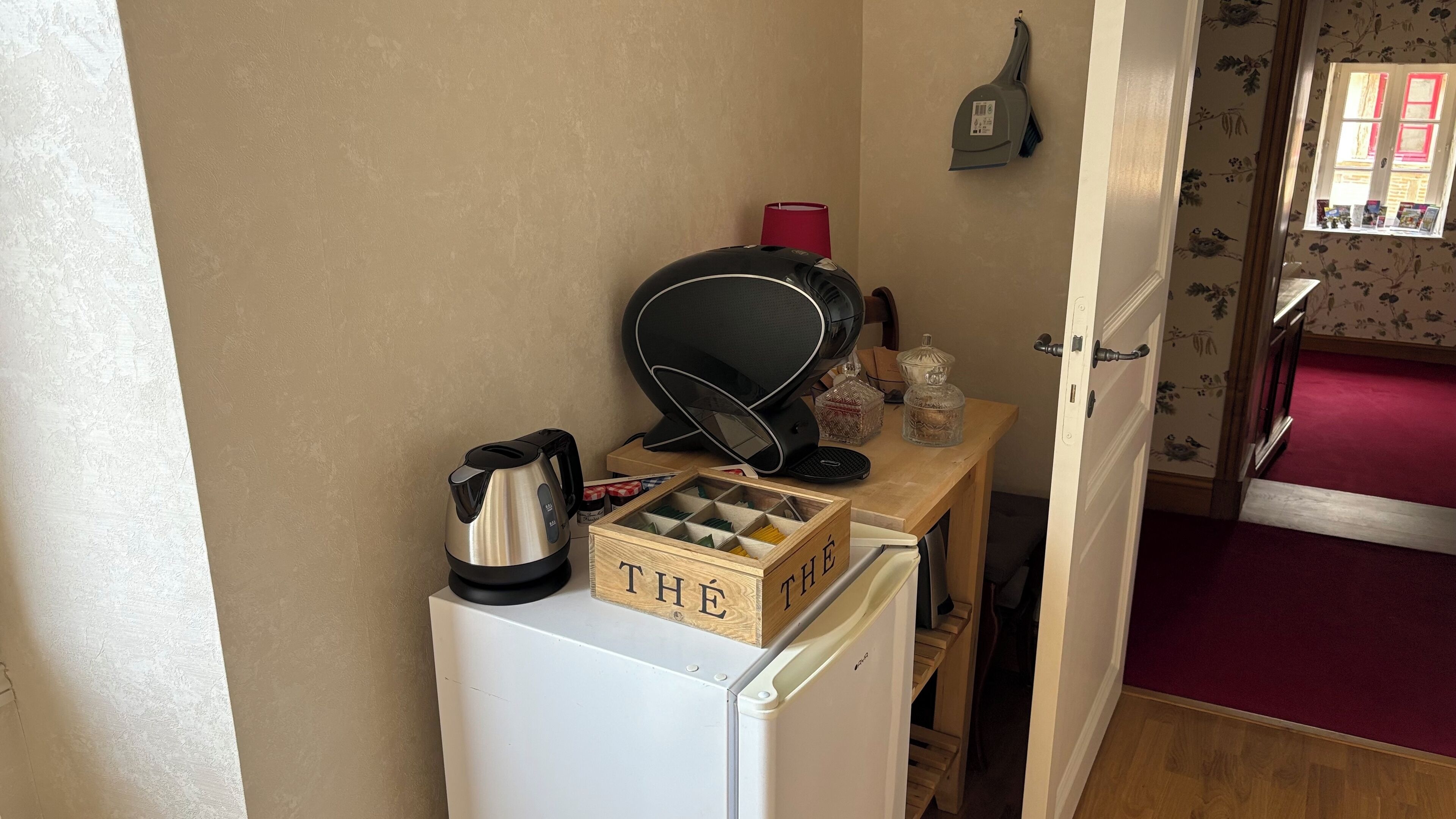 A compact kitchenette with a kettle, a coffee maker, and a wooden box labeled "THE HÉ".