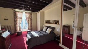 Un dormitorio con una cama grande, un aparador, una mesita de noche, un espejo y una ventana con cortinas.