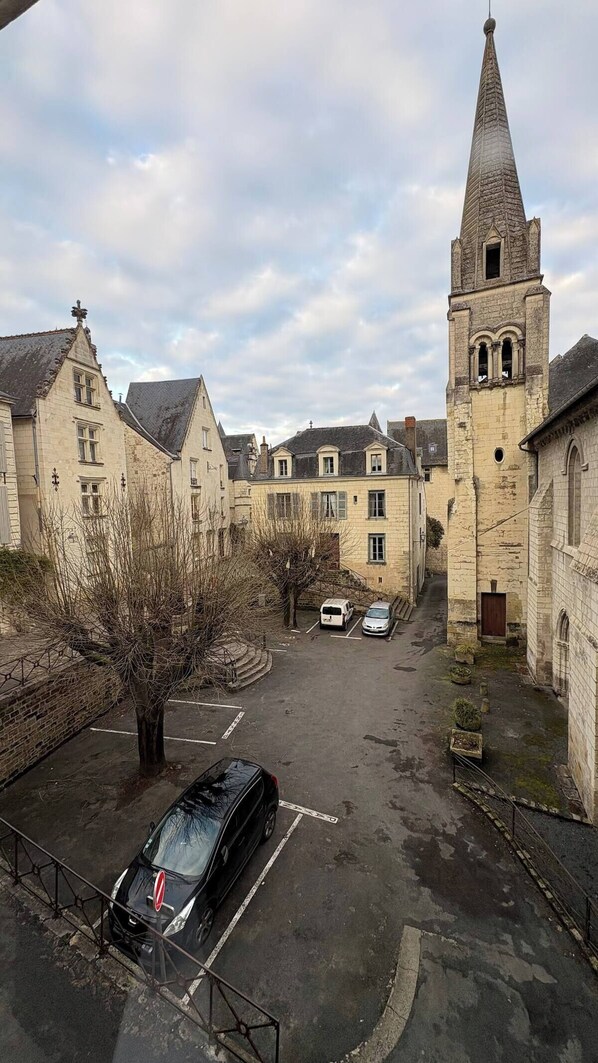 A narrow street with historic buildings, a church tower, and parked cars.