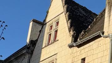 Ein historisches Gebäude mit einem steilen Satteldach, einem markanten Kreuz auf dem Dachfirst und einer roten Tür.