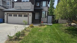 A two-story house with a garage, a stone facade, and a well-maintained lawn. - Big Family & Group-Friendly 9BR Home in NW Calgary (Calgary)
