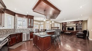 A spacious kitchen with a central island, wooden cabinets, and a dining area with a chandelier. - Big Family & Group-Friendly 9BR Home in NW Calgary (Calgary)
