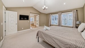 A bedroom with a large bed, a TV, a chandelier, and a window with curtains. - Big Family & Group-Friendly 9BR Home in NW Calgary (Calgary)