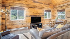 A log cabin interior with a television, leather sofa, dining table, and chairs.