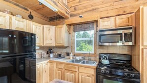 A kitchen with wooden cabinets, a black stove, a microwave, and a sink.