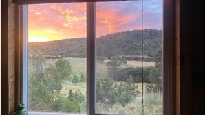 A window with a view of a sunset over a hilly landscape.