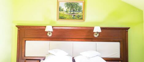 A bedroom with a wooden headboard, two bedside lamps, a bed with white linens, and a framed landscape painting on the wall.