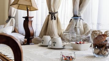 A dining table with a lace tablecloth, a lamp, teacups, a vase with dried flowers, and a bowl of candy.