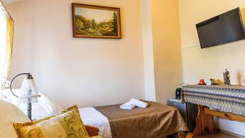 Una camera d'albergo con un letto, un tavolino con tovaglia decorativa, una televisione fissata al muro e un quadro sopra il letto.