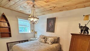 Une chambre à coucher avec un plafond en bois, un lustre, un lit avec une literie à motifs, une armoire en bois et un tableau encadré au mur.