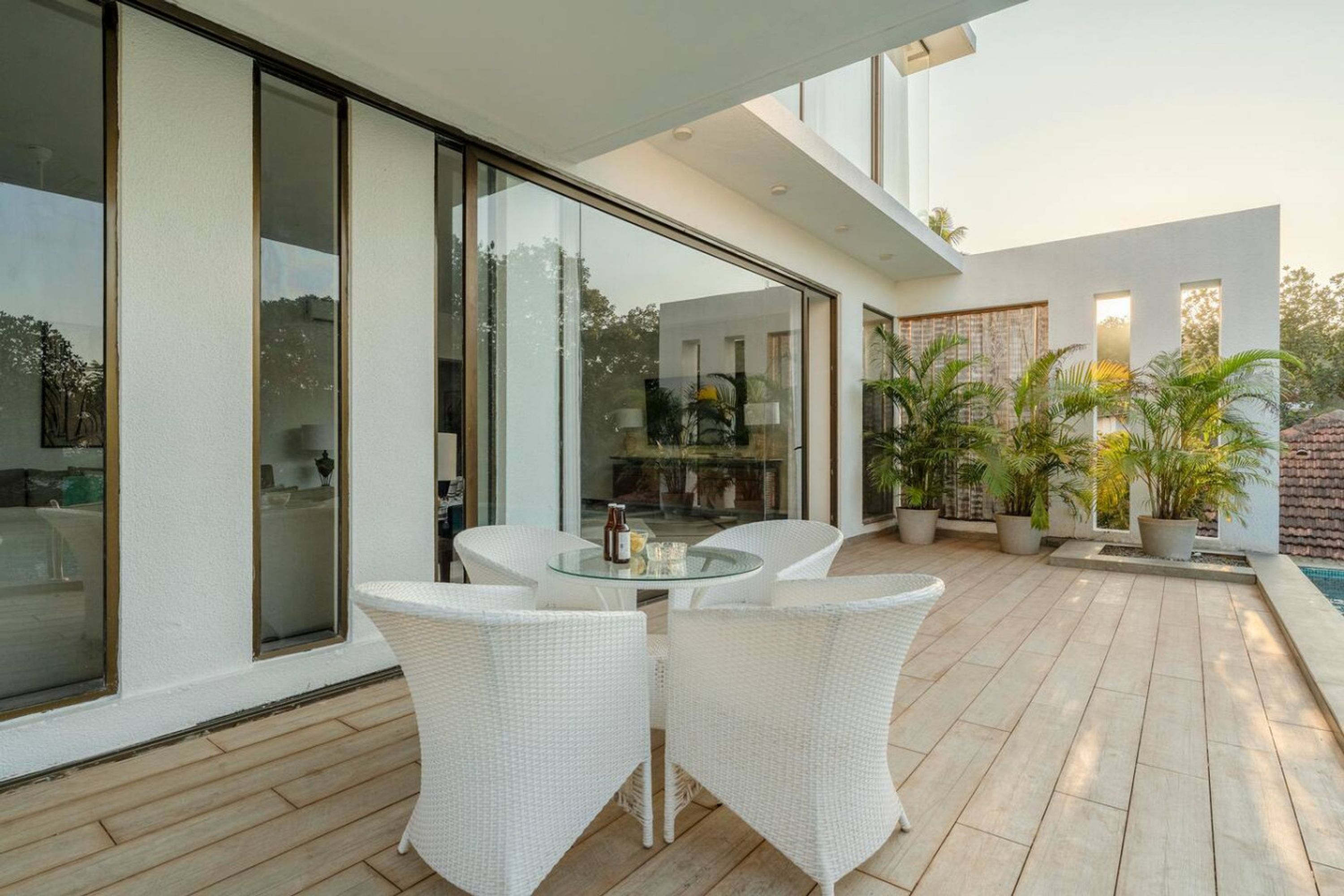 Eine moderne Terrassenanlage im Freien mit einem Glastisch und Korbstühlen, umgeben von Blumentöpfen und einem Schwimmbad.