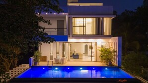 Ein modernes, zweistöckiges Haus mit Swimmingpool, Balkon und gut beleuchtetem Innenraum.