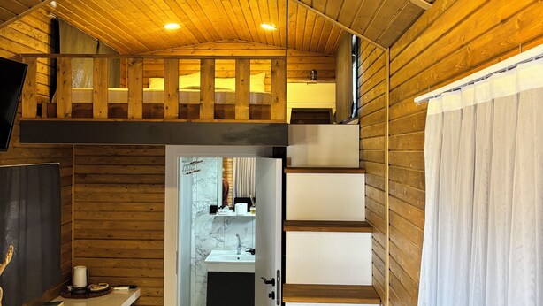 A compact, wooden cabin with a loft bedroom, a small kitchenette, and a bathroom.