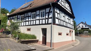 Une maison traditionnelle à colombages, avec un toit en pente, une cheminée visible et une petite entrée à l’avant.