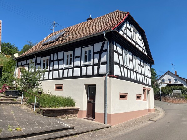 Ett traditionellt hus med korsvirkesfasad, ett sluttande tak, en synlig skorsten och en liten huvudentré.