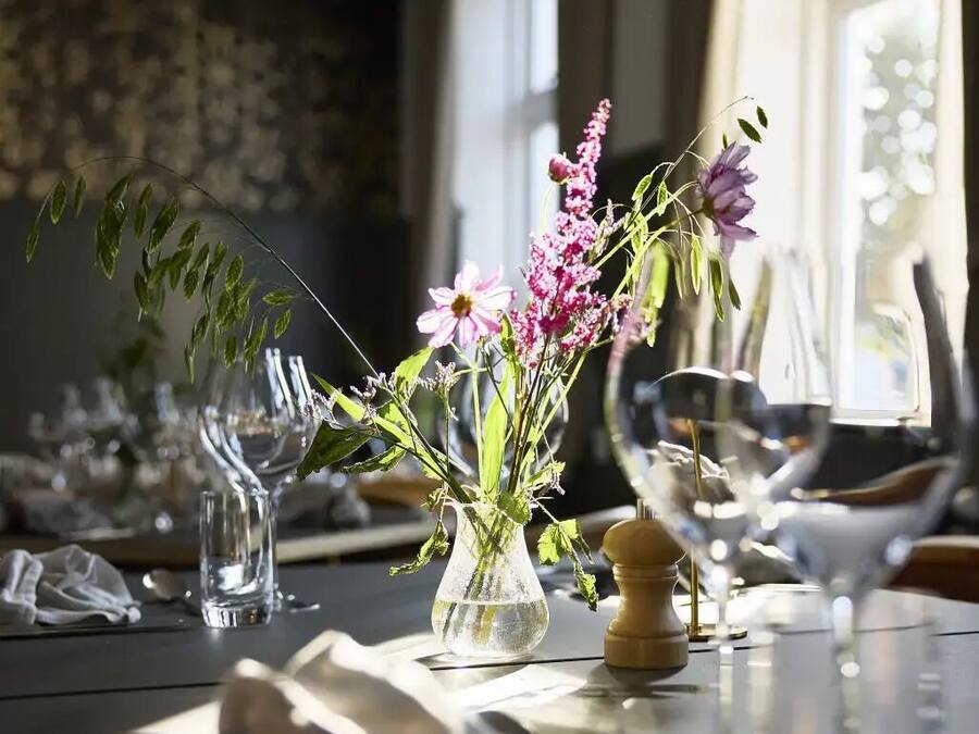 A dining table with a vase of flowers, glasses, and cutlery.