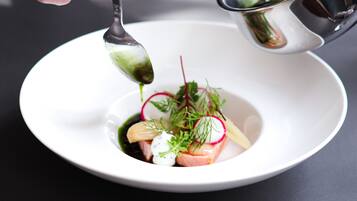 A person pouring a liquid from a metal bowl into a white plate with a spoon.