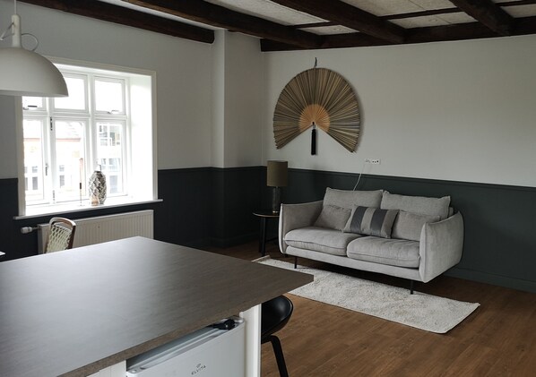 A modern living room with a grey sofa, a wooden coffee table, a white lamp, and a large wall fan. - Westergaards Hotel (Videbæk)