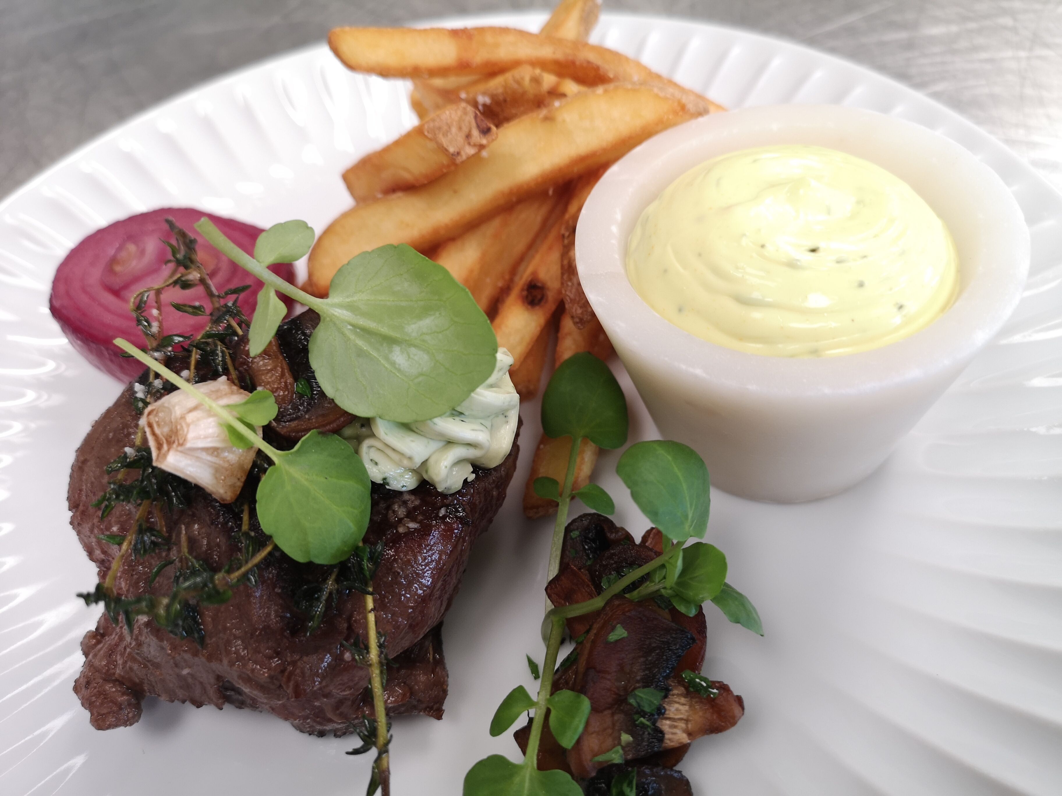 A plate with a steak, fries, and a creamy sauce.