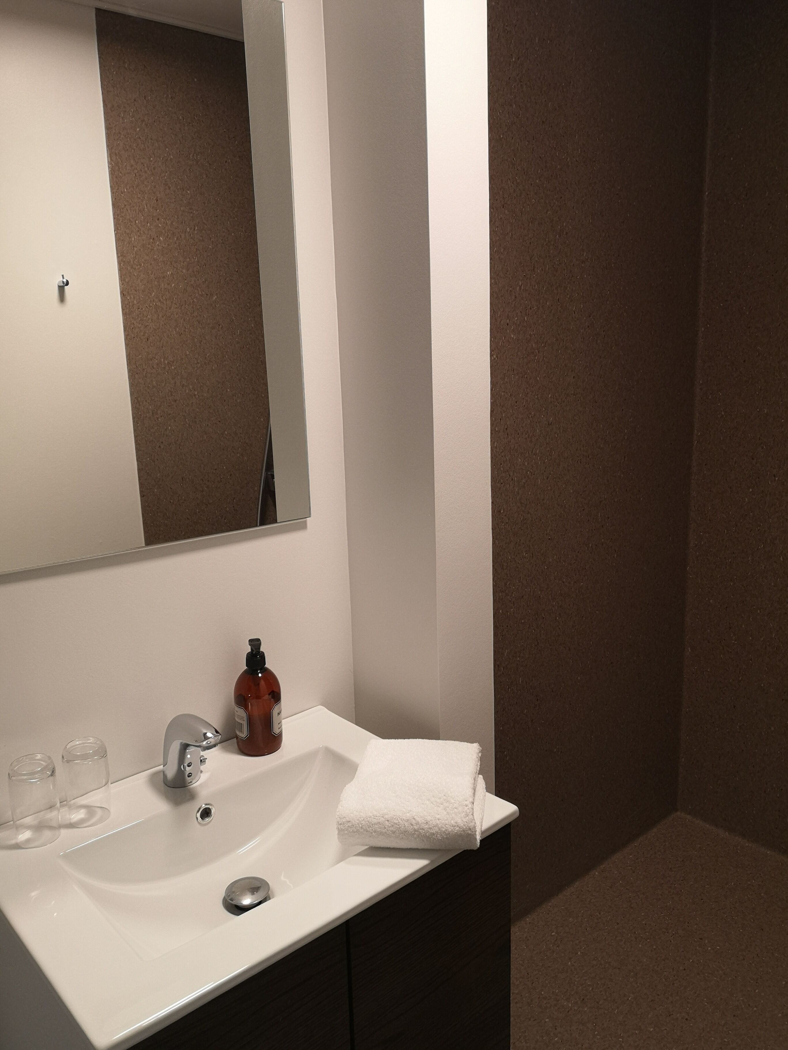 Une salle de bain avec un lavabo blanc, un miroir, un flacon de savon et une serviette.