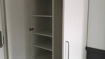 Un placard blanc, doté de plusieurs étagères et d’une poignée, situé dans une pièce dont le sol est recouvert de parquet.