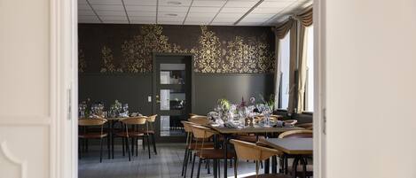 A dining area with tables set for a meal, wooden chairs, and a decorative wall with a floral pattern.