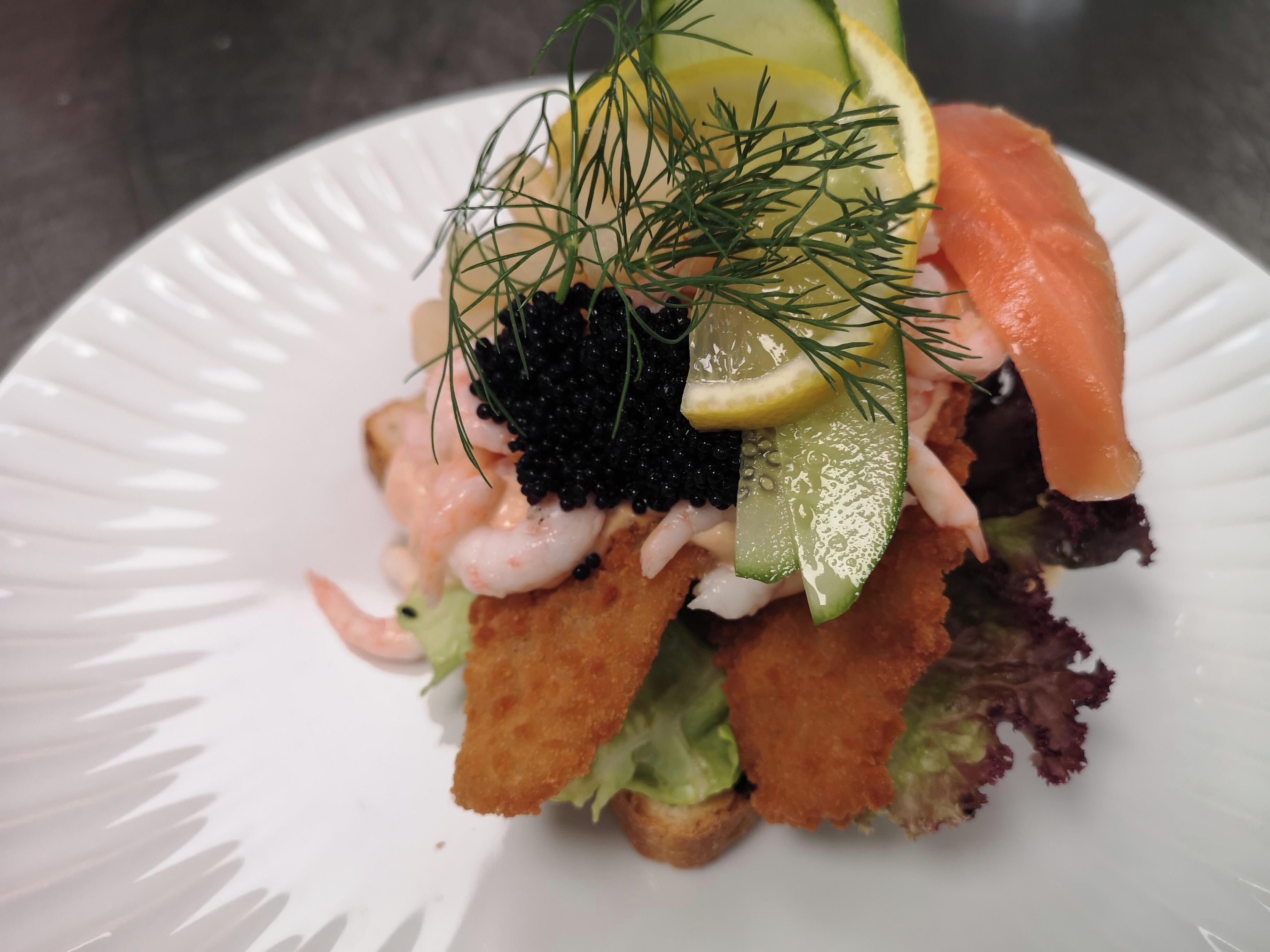 A seafood dish with shrimp, salmon, caviar, and garnishes on a white plate.