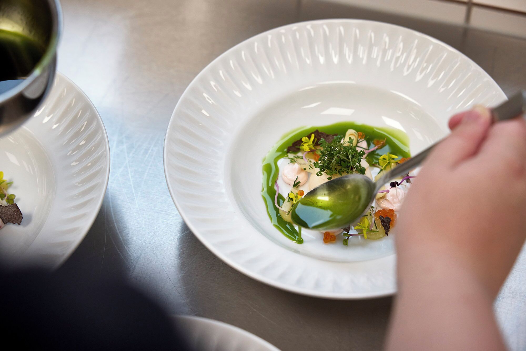 Una persona sirve un plato con una cuchara sobre un plato blanco.