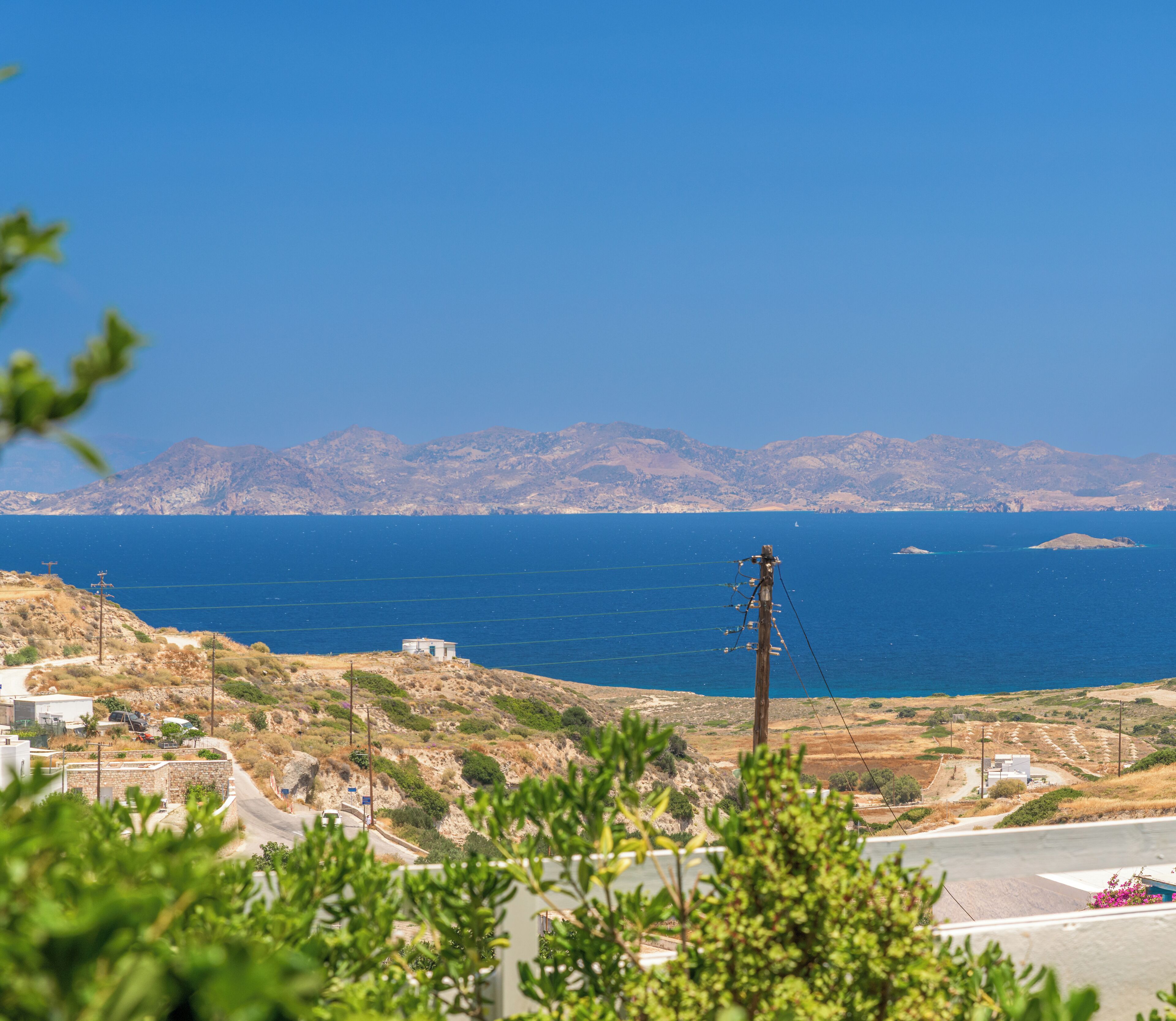 Un paysage côtier offrant une vue dégagée sur la mer, une petite île et des montagnes lointaines.