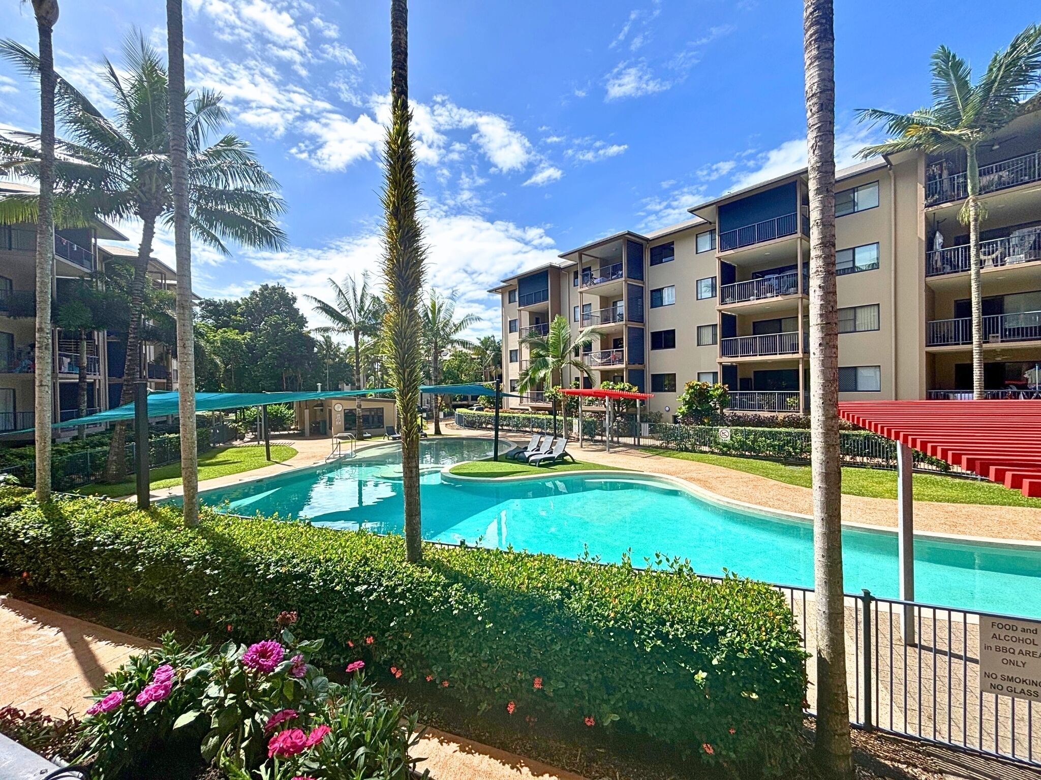 Une piscine entourée de palmiers et un immeuble à plusieurs étages doté de balcons.
