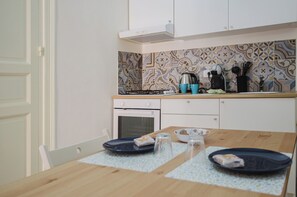 Une cuisine avec des meubles blancs, un pare-feu décoré et une table en bois surmontée d’un set de table bleu.
