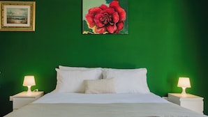 Ein Bett mit weißen Laken, zwei Nachttischlampen und ein gerahmtes Bild von einer roten Blume an einer grünen Wand.