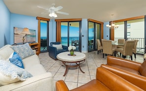 A living room with a sofa, a coffee table, and a TV. There are two doors leading to a balcony with a view of the ocean. - Phoenix Iv 4111 3 Bedroom Condo (Orange Beach)