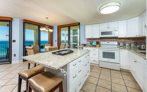 A kitchen with a large island, white cabinets, a microwave, and an oven. There is a balcony with a view. - Phoenix Iv 4111 3 Bedroom Condo (Orange Beach)