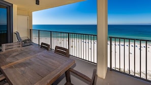 A balcony with a wooden table and chairs, overlooking a beach with umbrellas and people. - Phoenix Iv 4111 3 Bedroom Condo (Orange Beach)