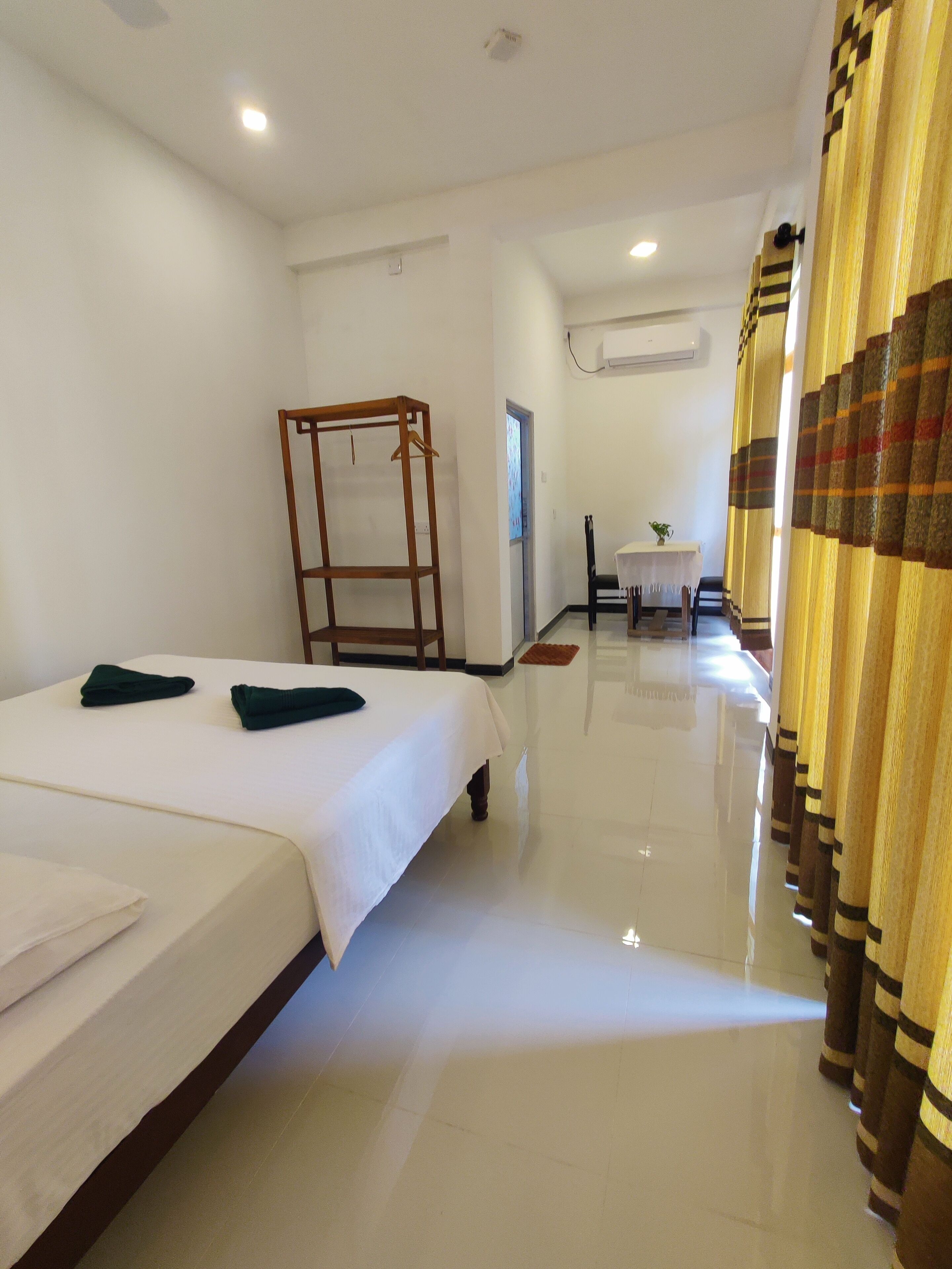 A hotel room with a bed, a wooden chair, a small table with a plant, and a window.