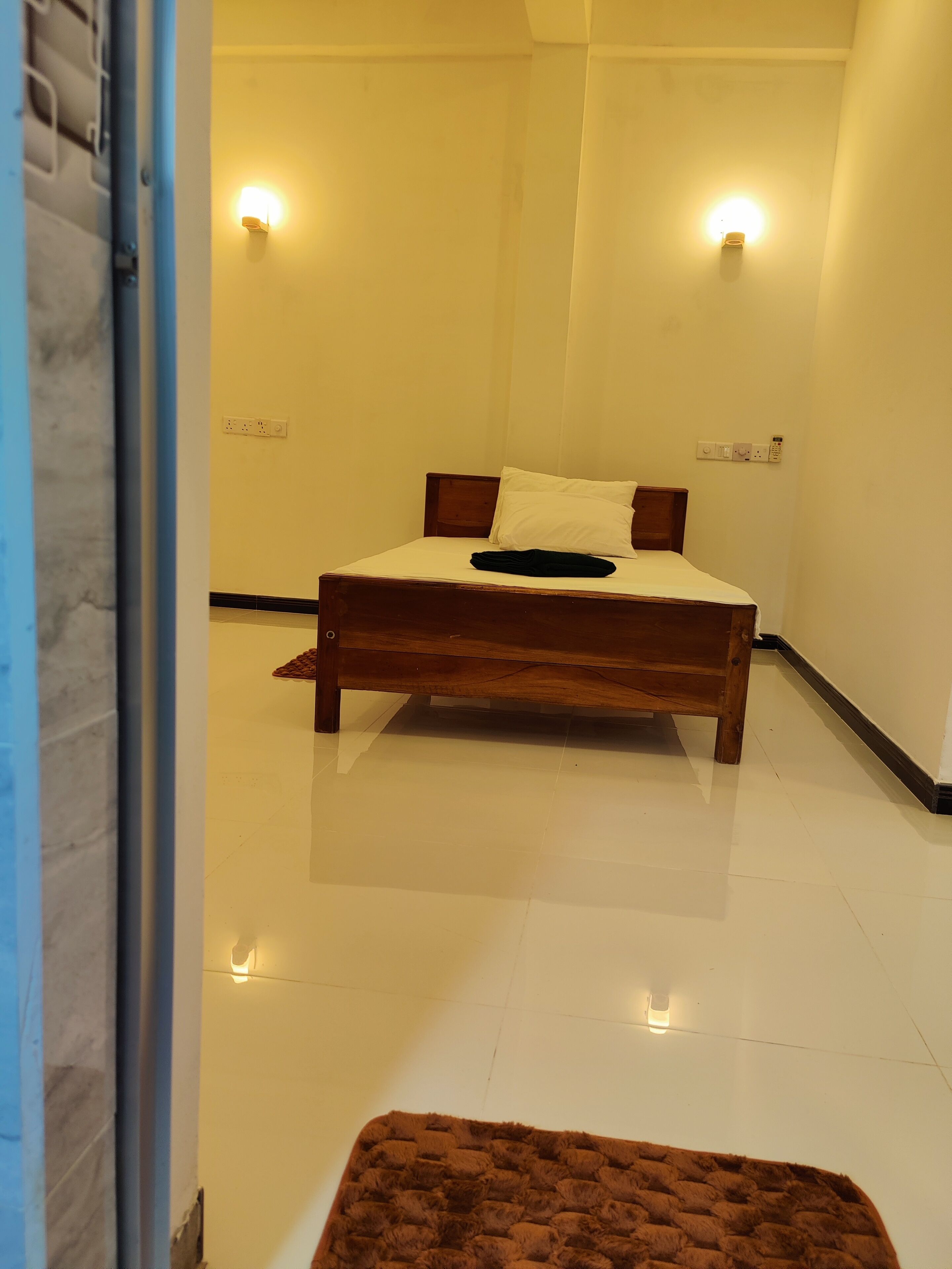 A bedroom with a wooden bed, white walls, and two wall-mounted lights.