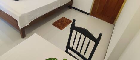 Una habitación pequeña y limpia con una cama, una mesa y una silla. Hay dos luces fijadas a la pared y una puerta.