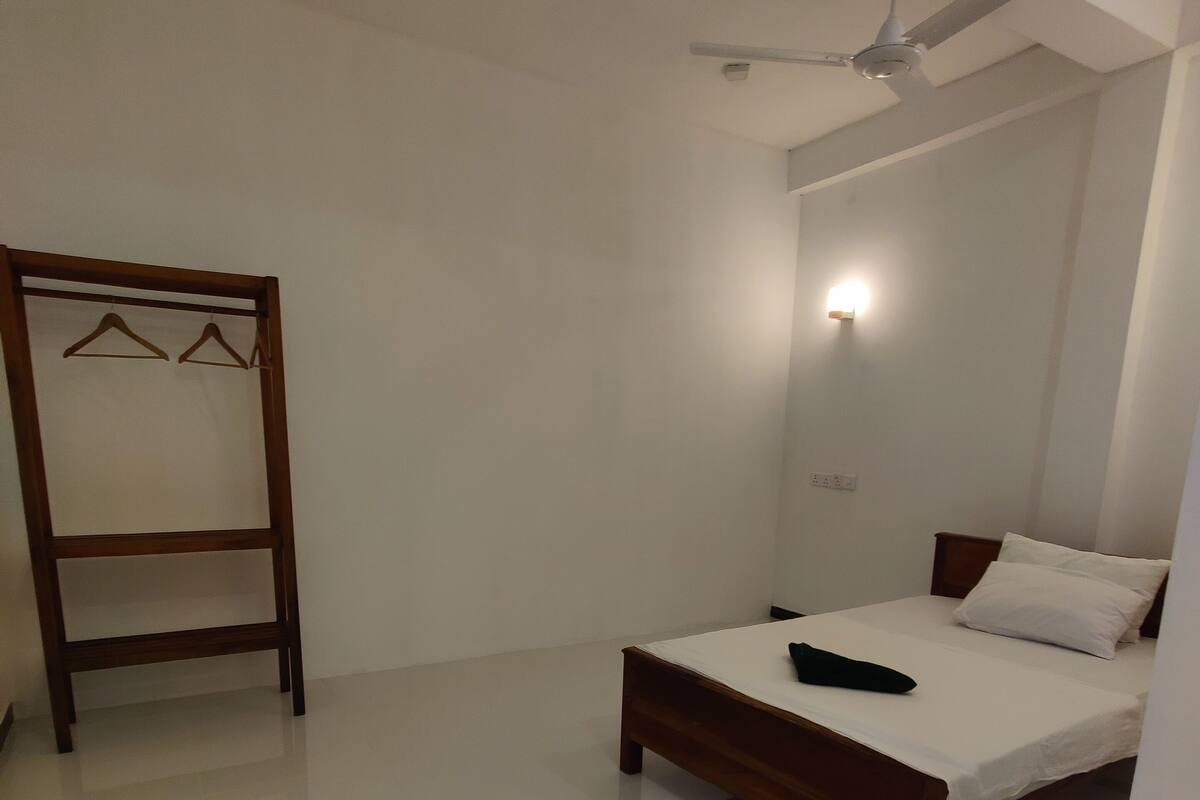 A bedroom with a bed, a wooden wardrobe, a ceiling fan, and a wall-mounted light.