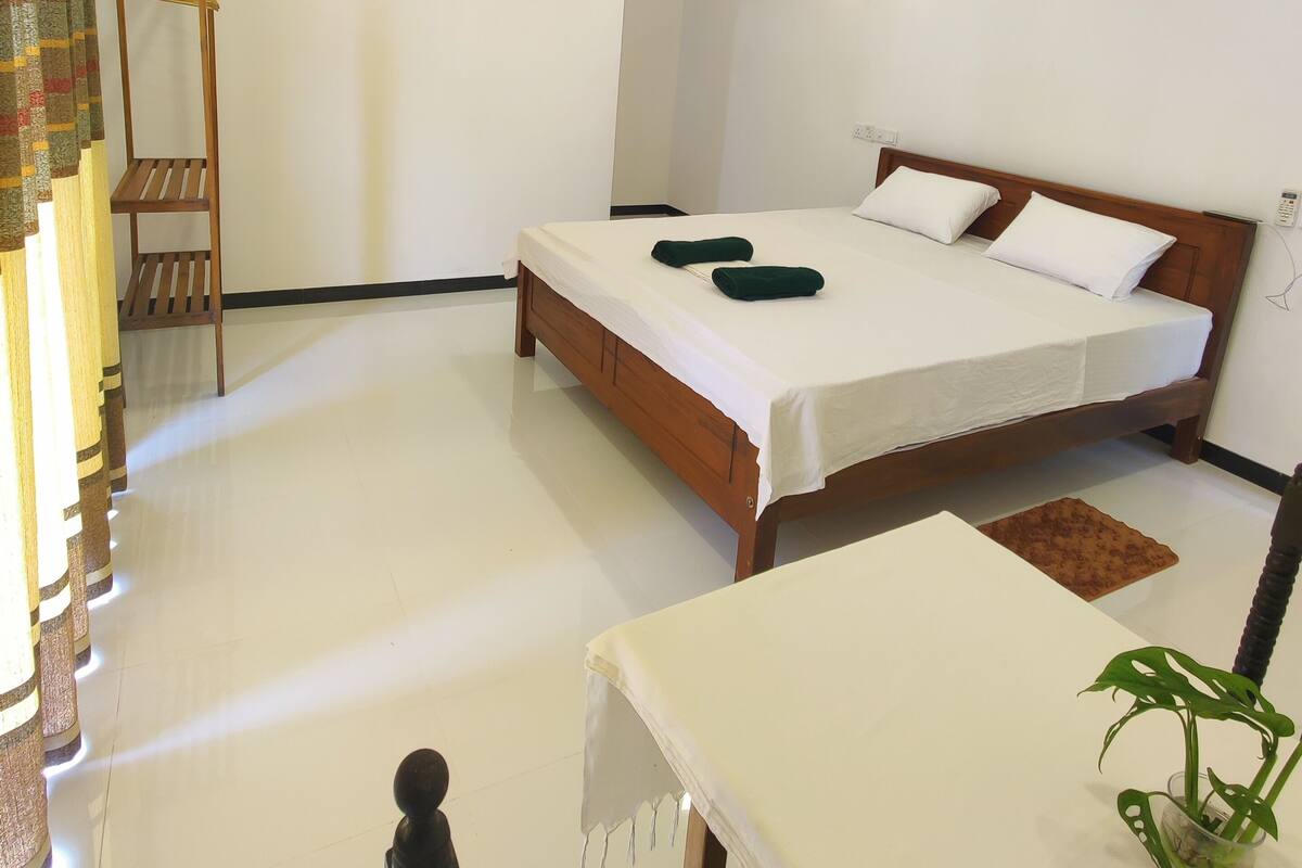 A bedroom with a wooden bed, white walls, a ceiling fan, and a small table with a plant.