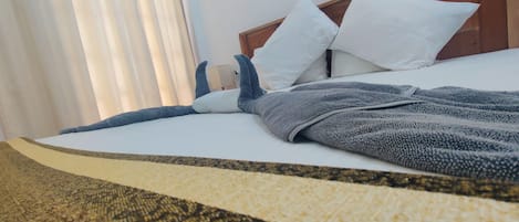 A bed with white linens, a grey blanket, and a wooden headboard.