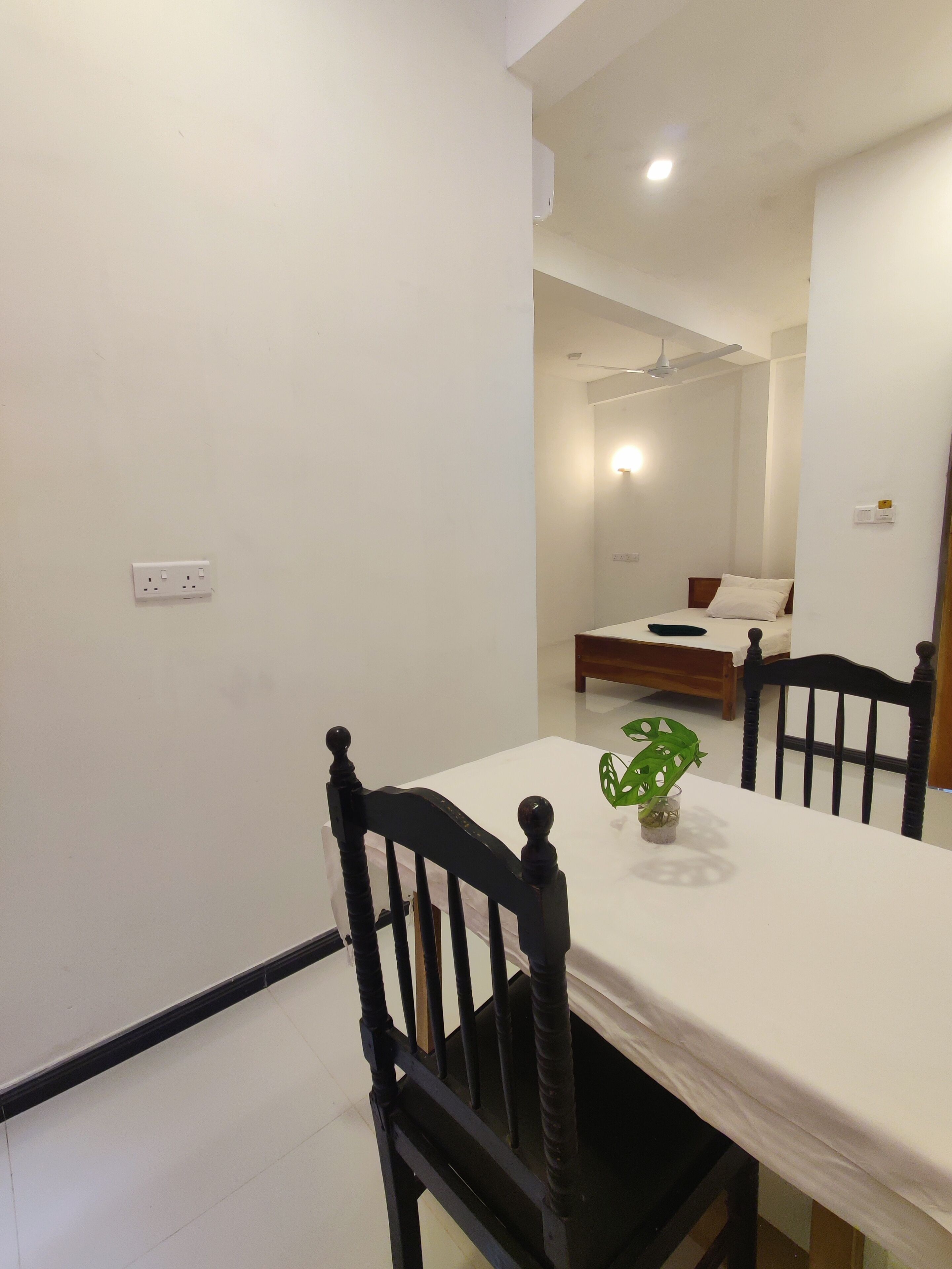 Un comedor con una mesa y sillas, un ventilador de techo y una cama al fondo.
