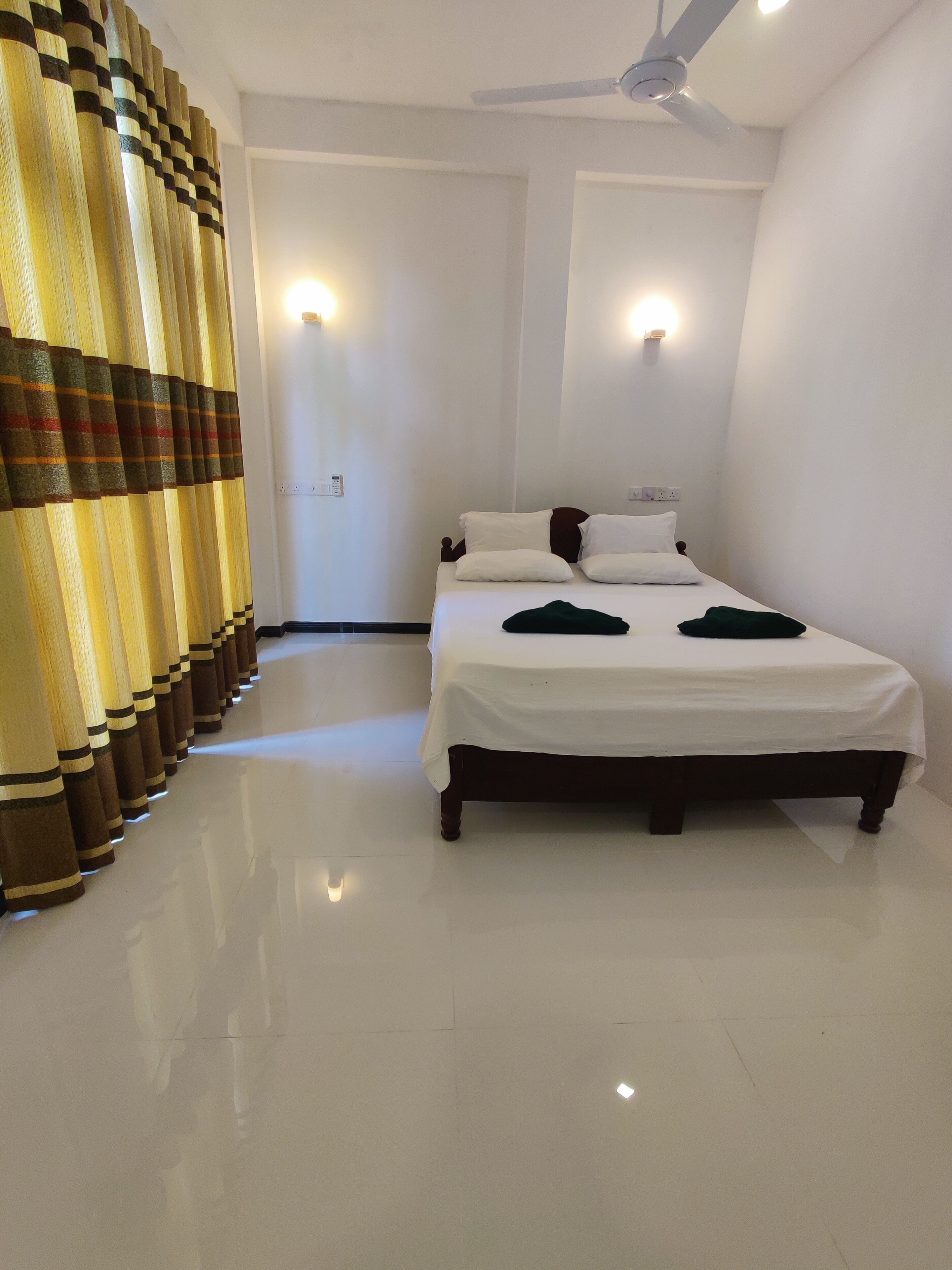 A hotel room with a bed, a ceiling fan, and a wall-mounted light fixture.