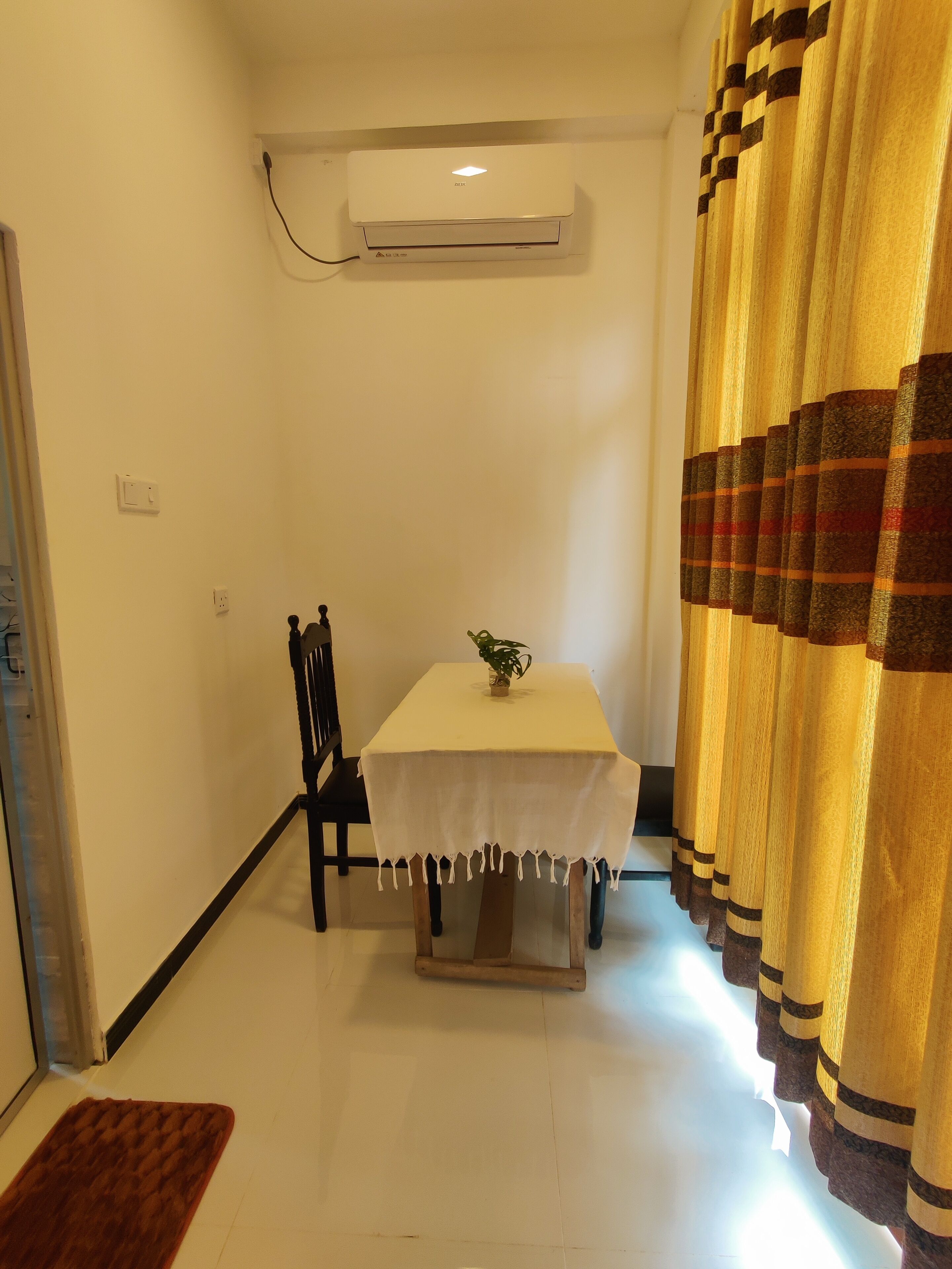 A small dining area with a table, chairs, an air conditioner, and a curtain.
