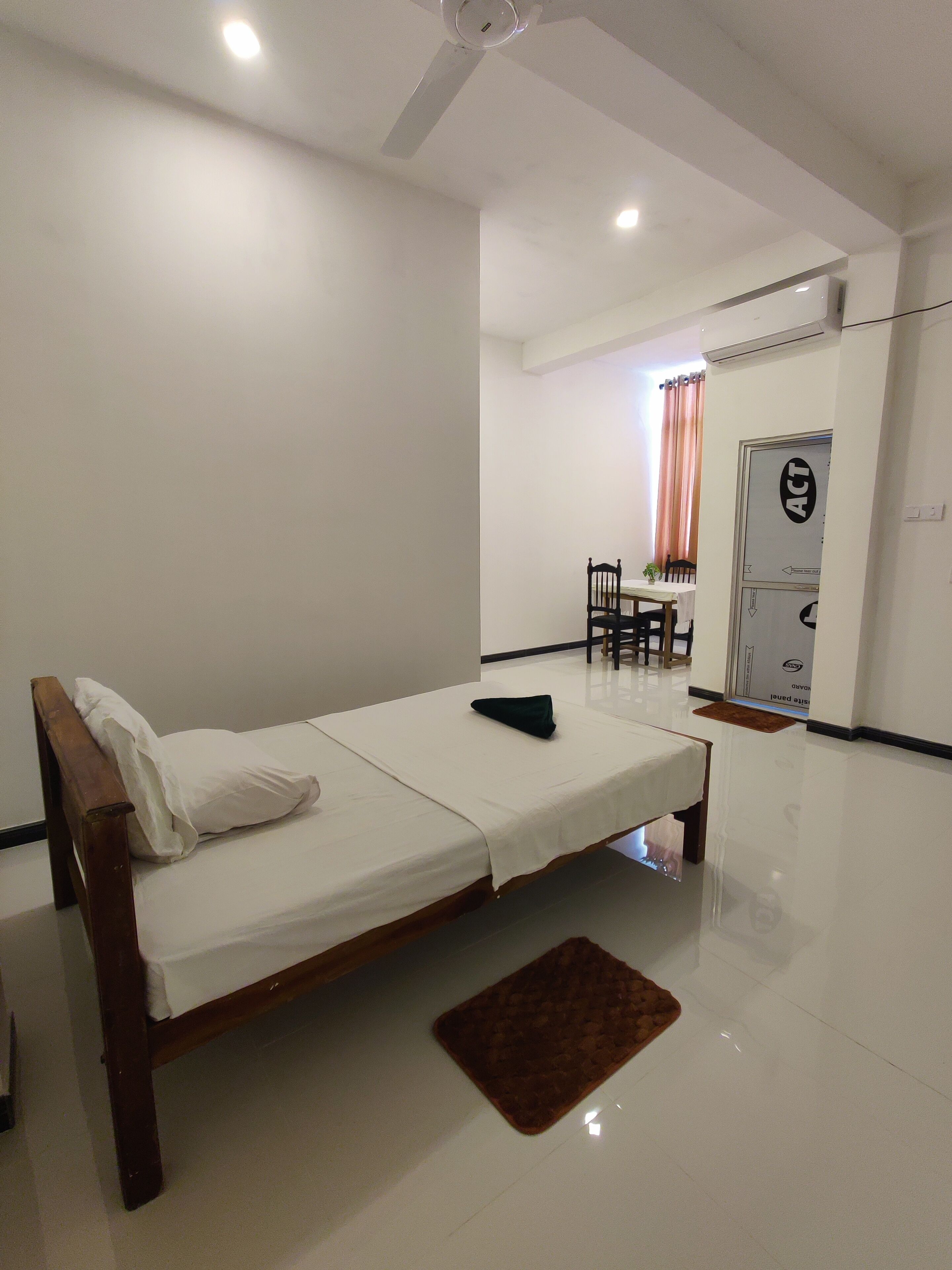 A room with a bed, a small table, and a chair. There is a door with a sign on it.