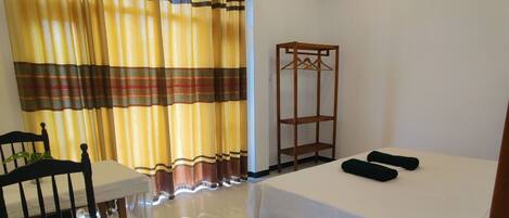 Ein Hotelzimmer mit einem Bett, einem Holzstuhl, einem kleinen Tisch und einem hängenden Regal.
