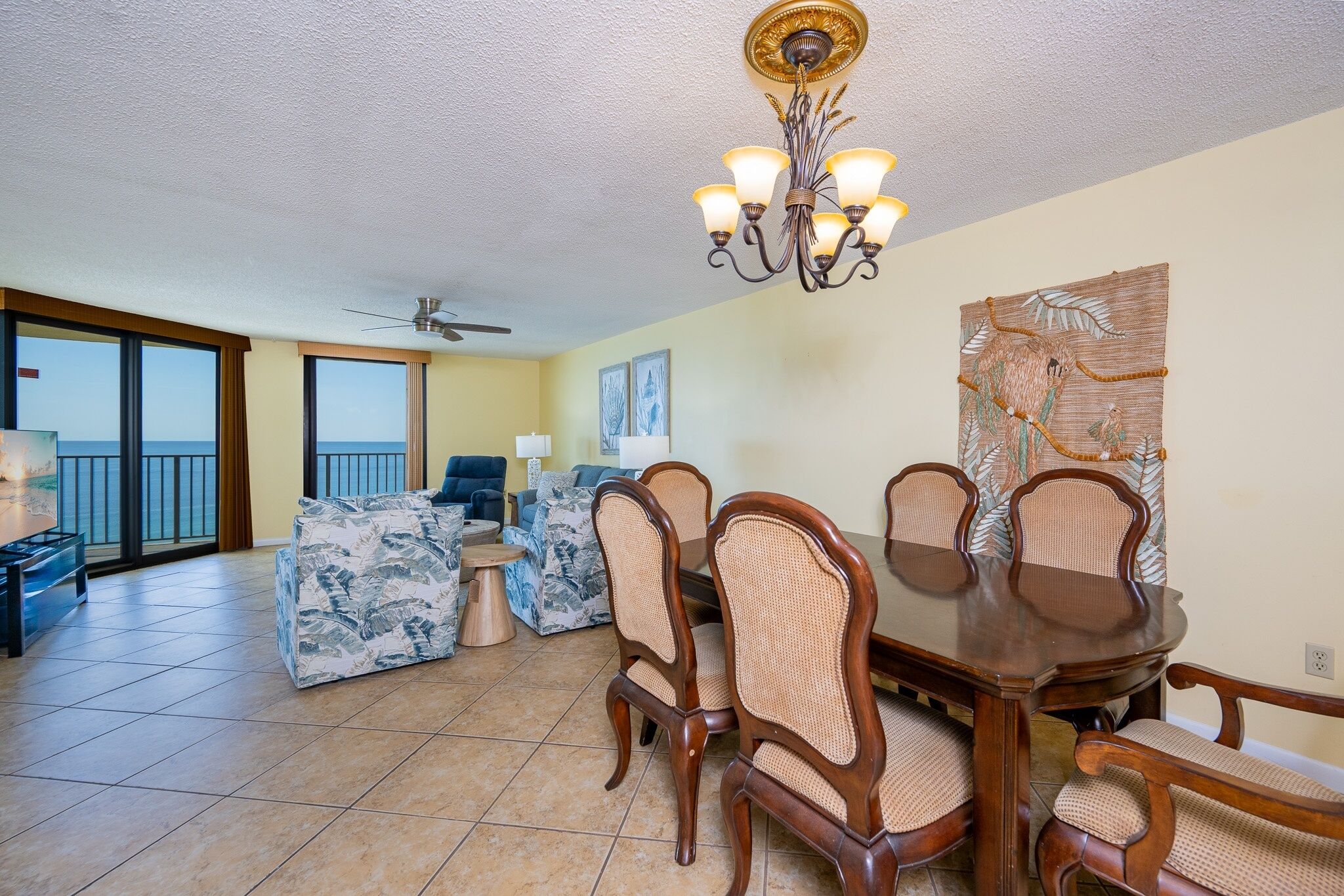 A spacious living room with a dining area, large windows, and a ceiling fan.