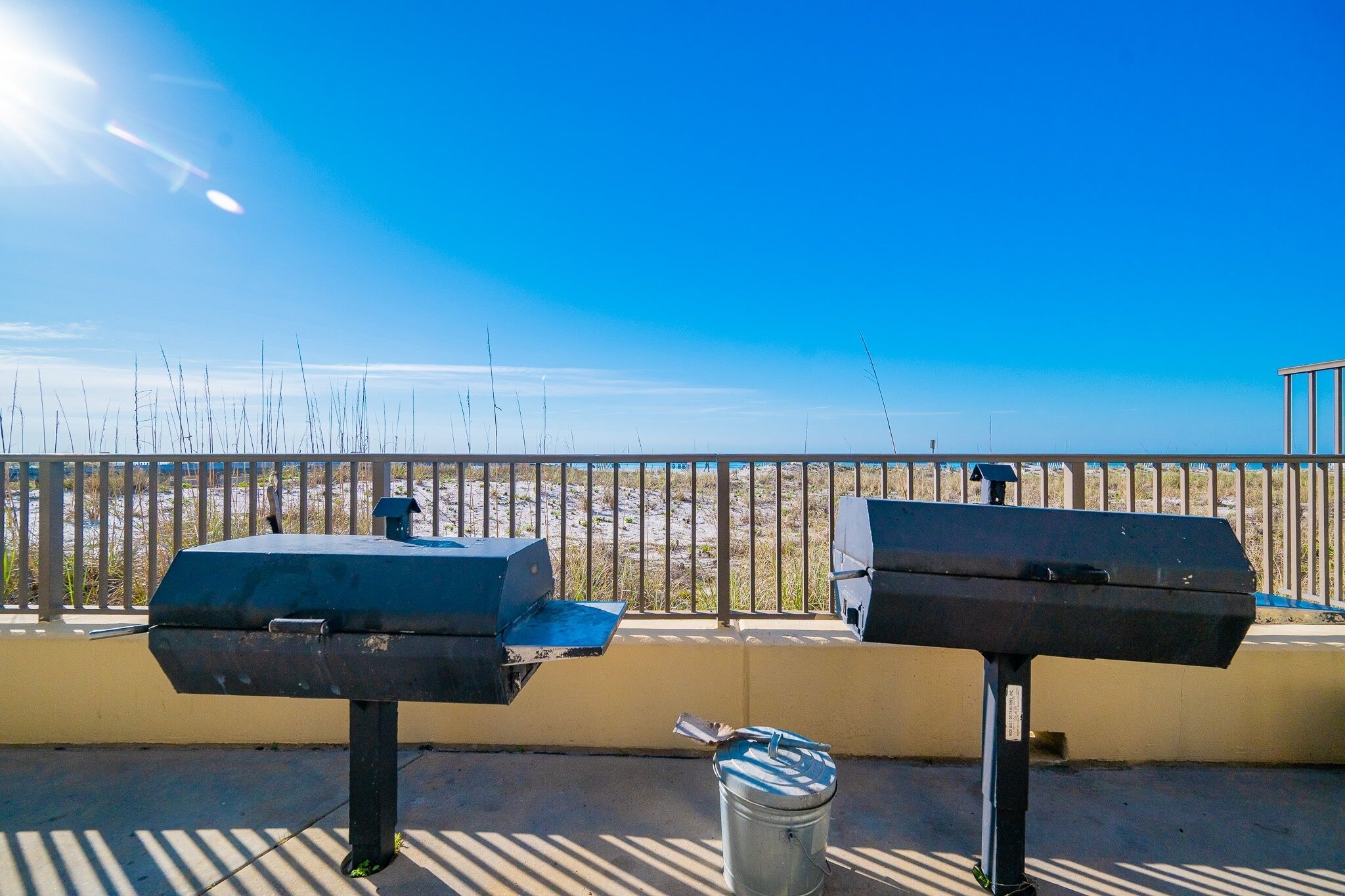 A barbecue grill and a trash can on a balcony with a view of the beach.