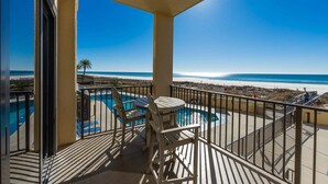 A balcony with a pool, chairs, and a view of the beach and ocean.